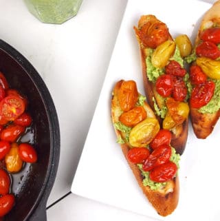 Tomatoes on bread slices with whipped feta and a cast iron pan with cooked tomatoes on the side.