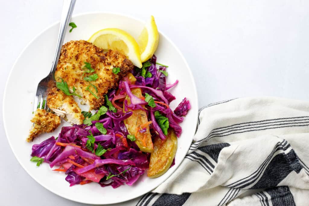 Air fryer schnitzel on a white plate with the sweet and sour cabbage with a napkin on the side on a white background