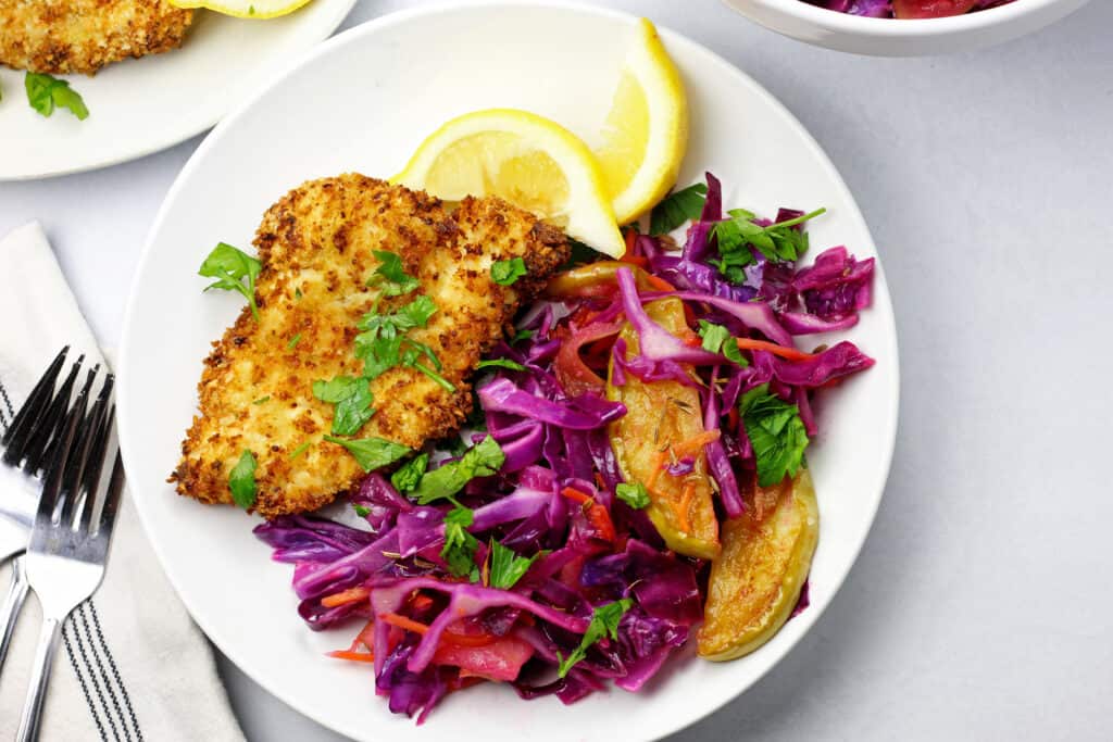 Close up of the air fryer schnitzel with the cabbage on a plate with lemon slices