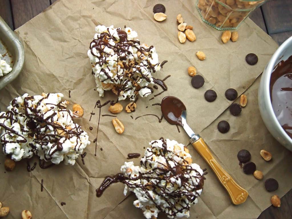 Three popcorn clusters on brown paper with chocolate drizzle and peanuts