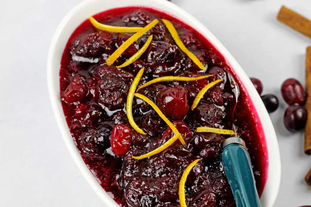 Close up of the best ever cranberry sauce with orange zest on a white background with a blue spoon.