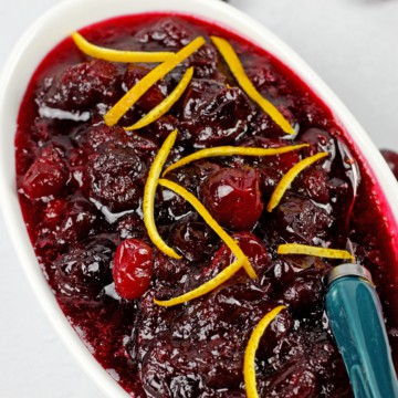 Close up of the best ever cranberry sauce with orange zest on a white background with a blue spoon.