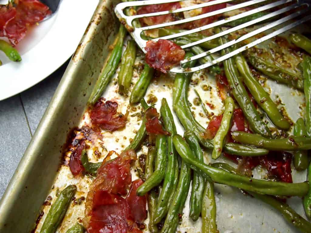 close up of a sheet pan with crispy green beans and prosciutto with mustard vinaigrette