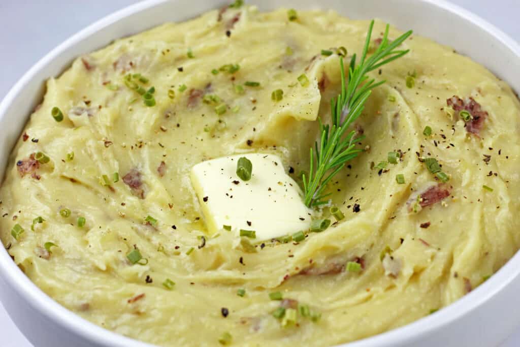 Close up of red skin mashed potatoes with a pat of melting butter and sprig of rosemary on top.