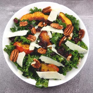 Overview of roasted acorn squash on top of massaged kale salad with pecans, shaved Parmesan, and dried cranberries in a bowl