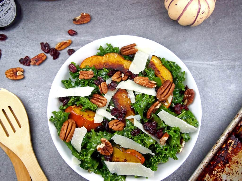 Roasted acorn squash on top of massaged kale salad with pecans, shaved Parmesan, and dried cranberries with serving utensils