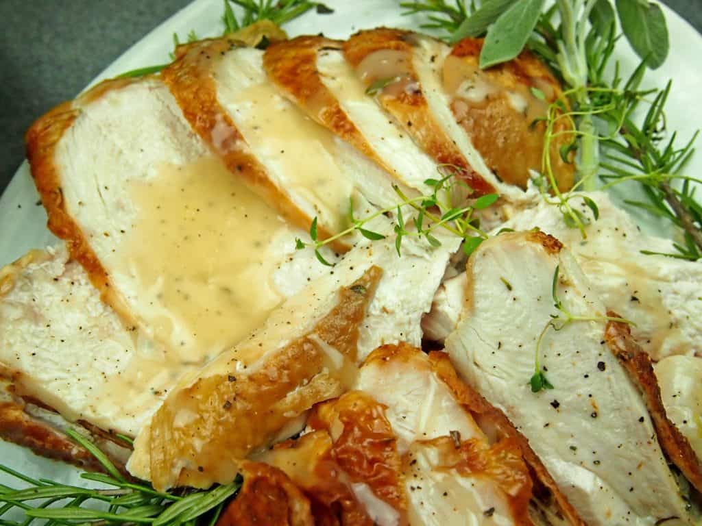 Overview of a platter of roasted turkey breast with gravy and herbs