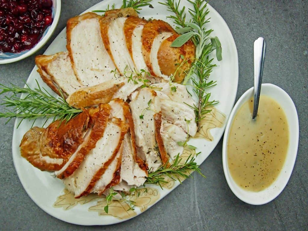 Overview of roasted turkey breast on a platter with gravy and cranberry sauce on the side