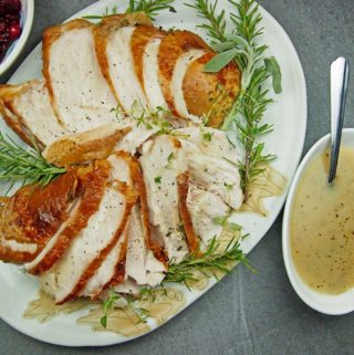 Overview of roasted turkey breast on a platter with gravy and cranberry sauce on the side