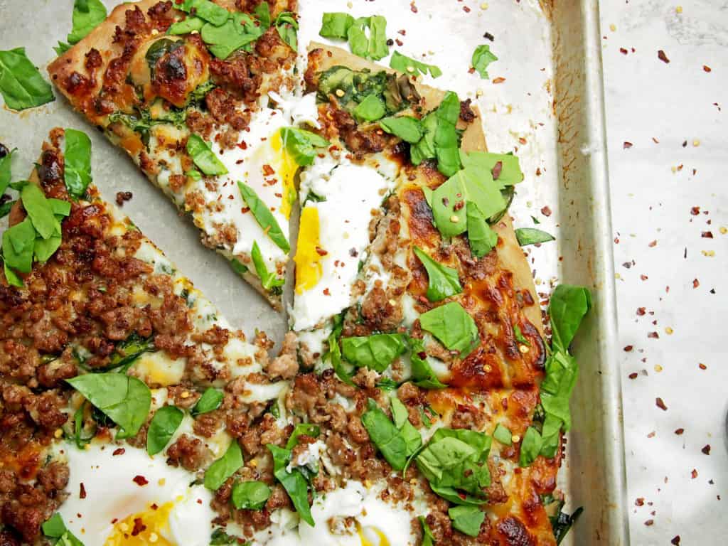 Overview of a sliced pizza with drippy eggs, sausage, and spinach on top.