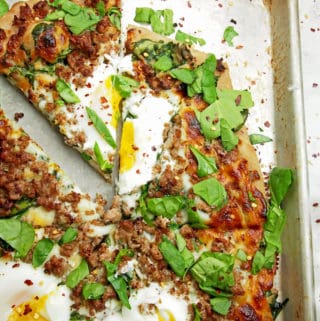 Overview of a sliced pizza with drippy eggs, sausage, and spinach on top.