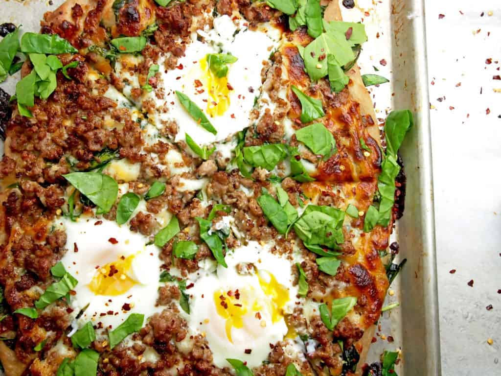 Close up of a pizza with drippy eggs, sausage, and spinach on top.