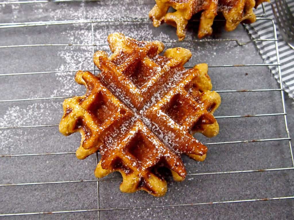 Close up of an eggnog waffle on a cooling rack dusted with powdered sugar