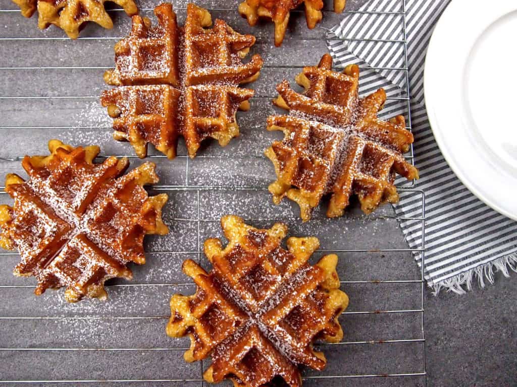 Overview of eggnog waffles cooling on a rack dusted with powdered sugar