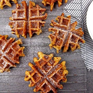 Overview of eggnog waffles cooling on a rack dusted with powdered sugar