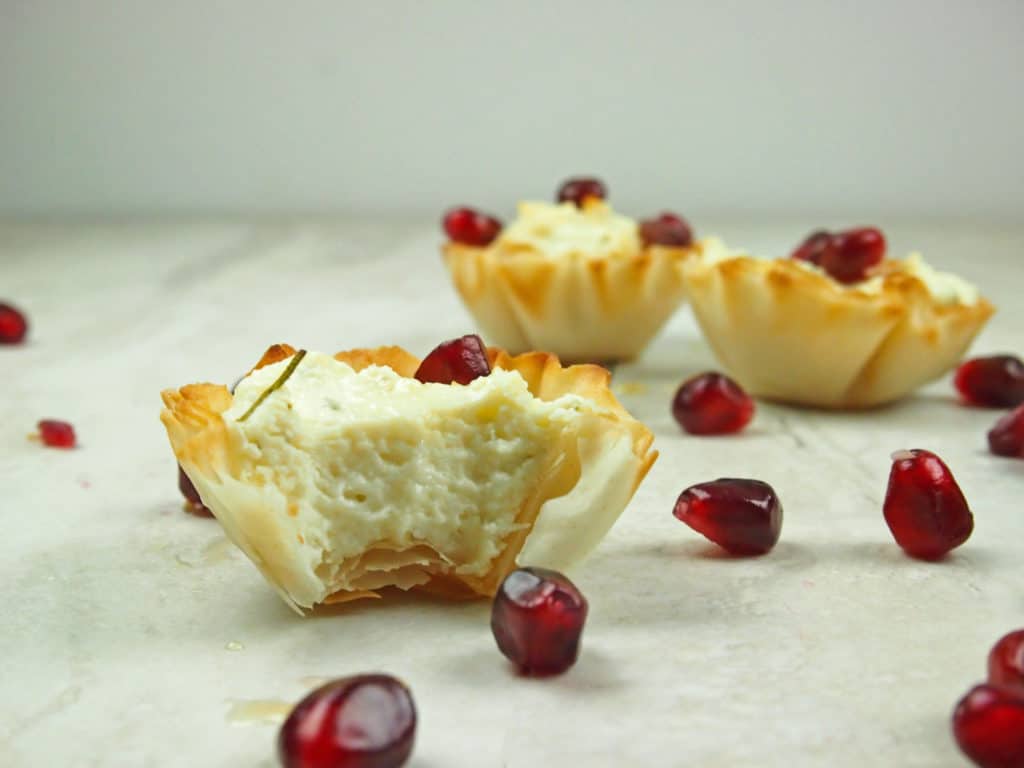 Close up of a bitten phyllo cup stuffed with whipped feta and pomegranate seeds
