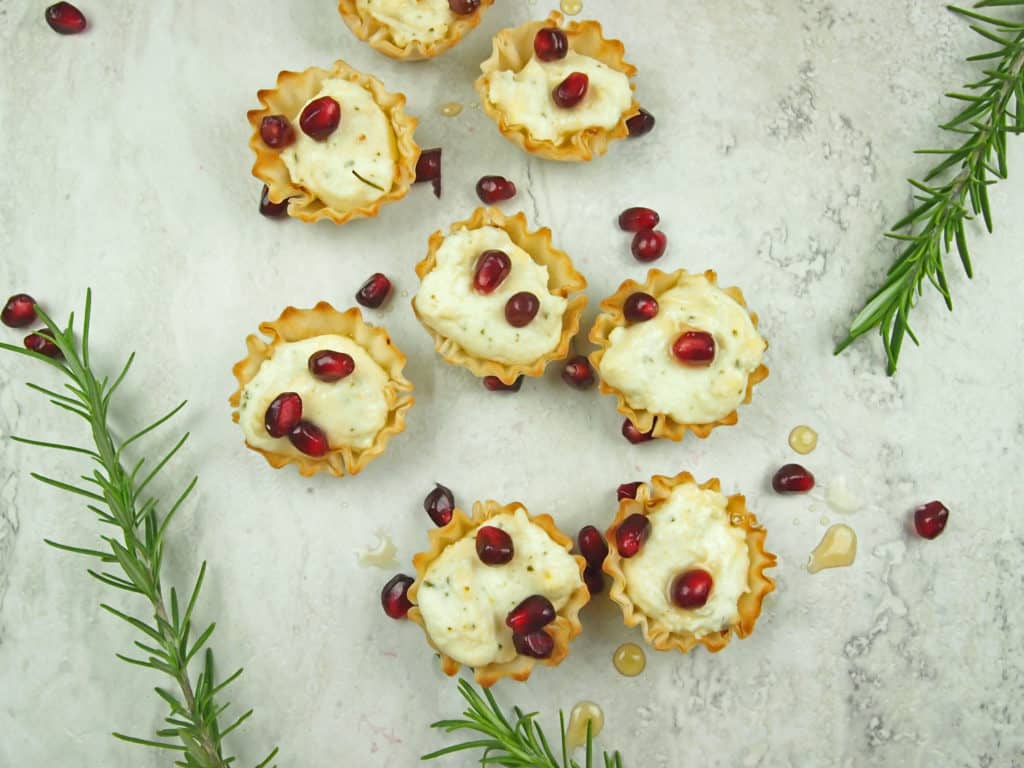 Overview of phyllo cups stuffed with whipped feta with pomegranate seeds and rosemary sprigs