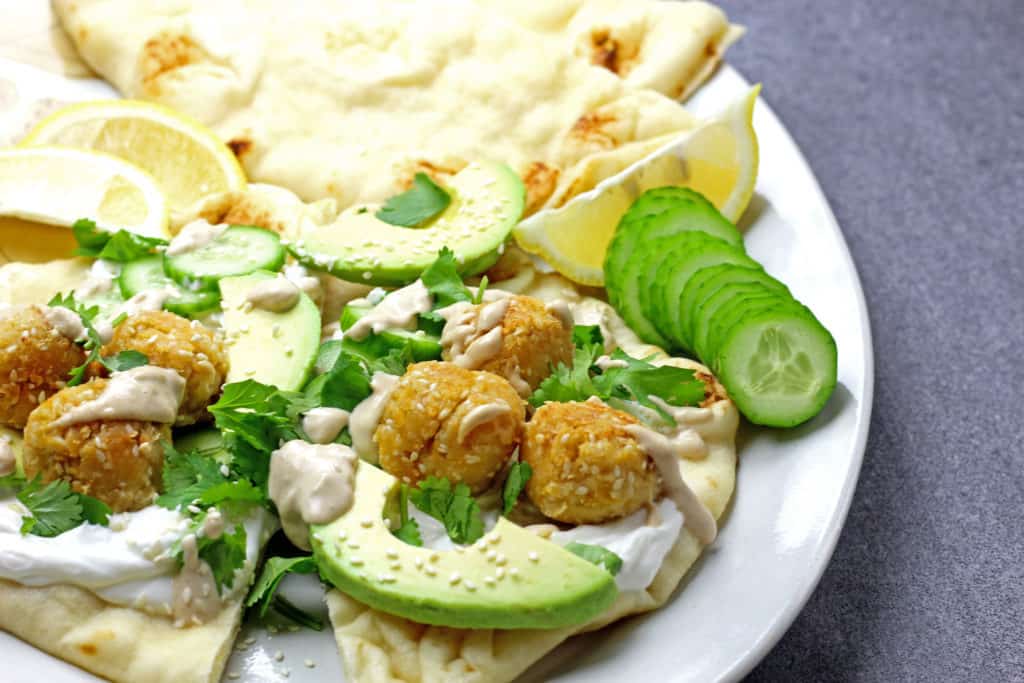 Sesame falafel with avocado, sesame seeds, and cucumber slices on a serving platter