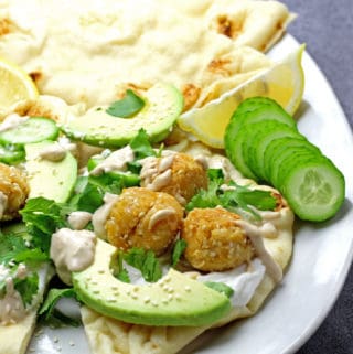 Sesame falafel with avocado, sesame seeds, and cucumber slices on a serving platter