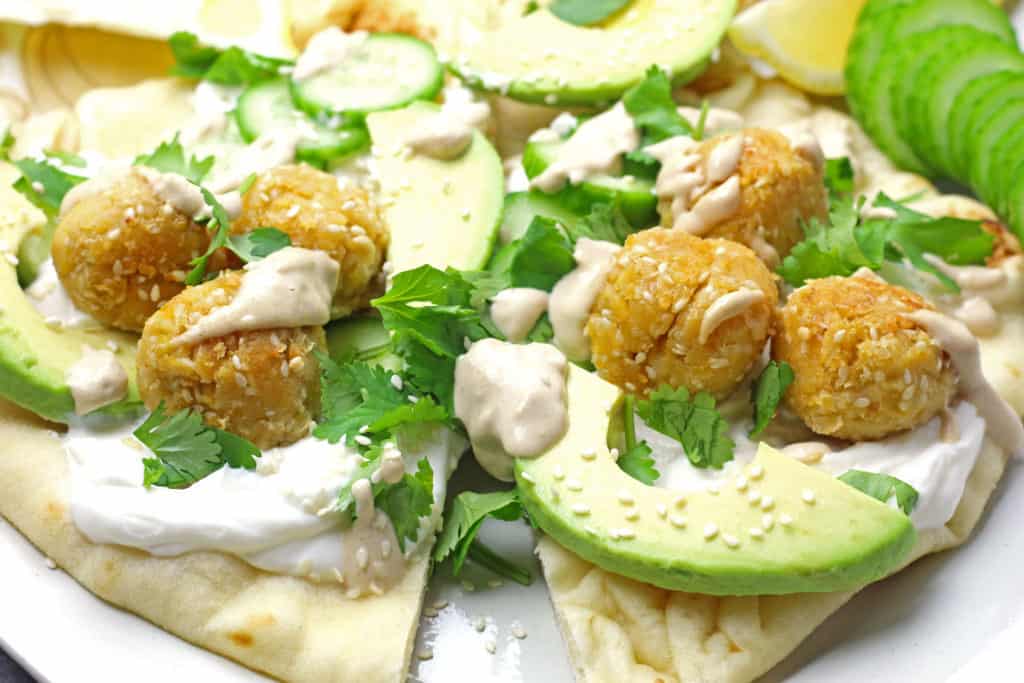 Close up of sesame falafel with avocado, cilantro, sesame seeds, and tahini drizzle