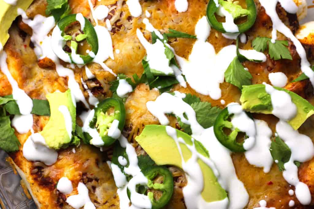 close up of the top of smoked chicken enchiladas with toppings of avocado, jalapenos, cilantro, and sour cream