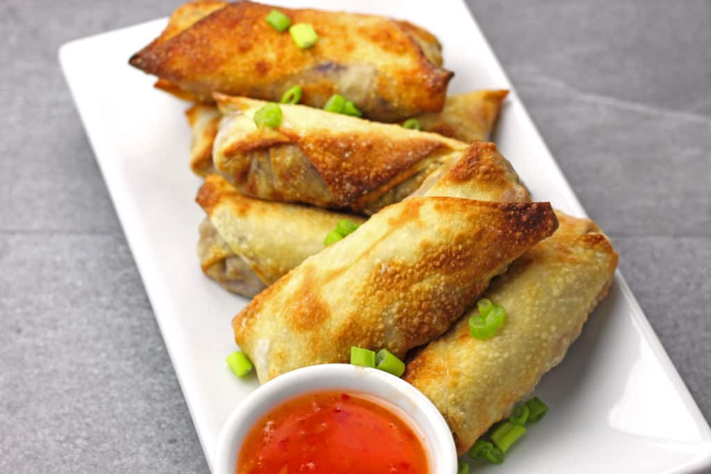 Air fryer egg rolls on a plate with dipping sauce on the side