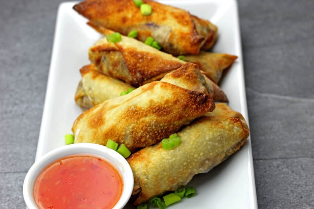 Air fryer egg rolls on a plate with dipping sauce on the side