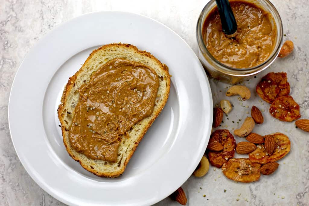 Banana nut butter on a piece of toast with a jar and nuts beside.