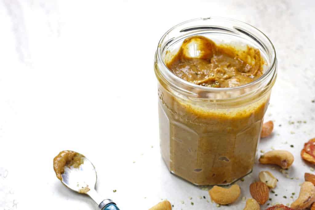 Jar of banana nut butter with a spoon on a white background.