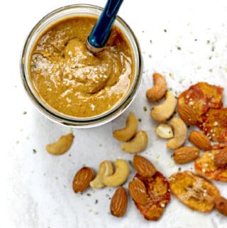 Overview of banana nut butter with a spoon in the jar with nuts and dried bananas scattered on a white background.