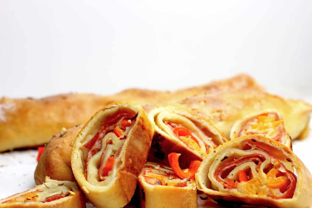 Sliced pepperoni rolls showing the pepperoni, cheese, and peppers in side on a white background.