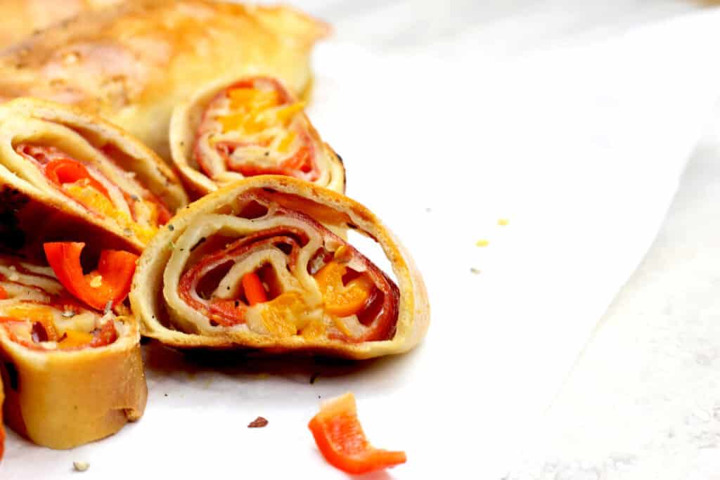 Close of up the pepperoni roll slices where you can see the pepperoni, cheese, and peppers inside on a white background.