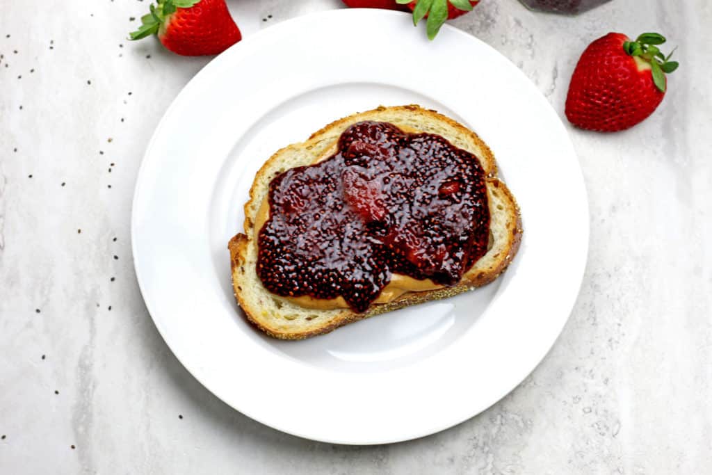 Overview of Balsamic Strawberry Chia Jam spread on a piece of bread with peanut butter and strawberries in the background