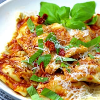 Close of vegetarian ravioli with basil and tomato sauce with red pepper flakes in background