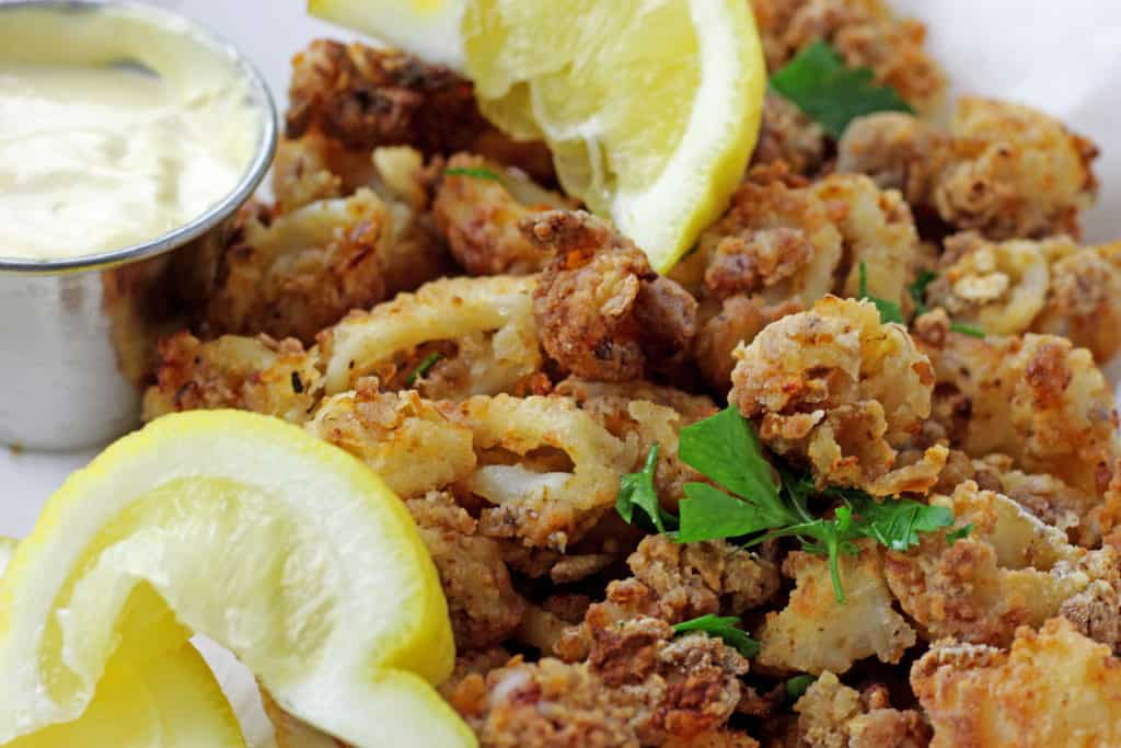 Close up of crunchy air fryer calamari with lemons, parsley, and mustard dipping sauce