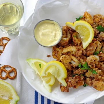 Overhead view of crunchy air fryer calamari in a bowl with lemons, parsley, and mustard dipping sauce served with white wine on the side.