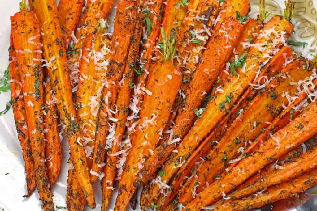 A close up of caramelized air fryer carrots on a plate topped with dill and parmesan