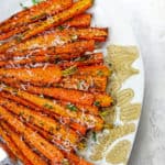 Caramelized air fryer carrots laid out on aplate topped with dill and parmesan