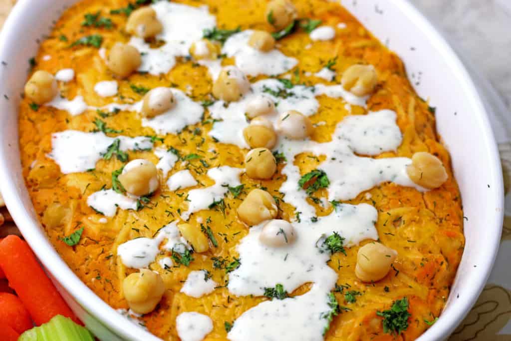 Close up of buffalo chickpea dip surrounded by veggies and crackers on a plate.