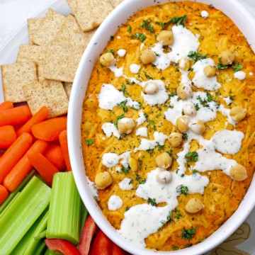 Buffalo chickpea dip surrounded by veggies and crackers on a plate.