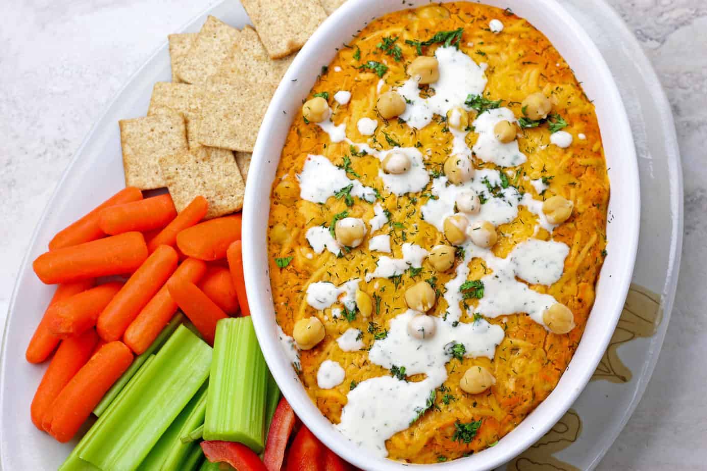 Buffalo chickpea dip surrounded by veggies and crackers on a plate.