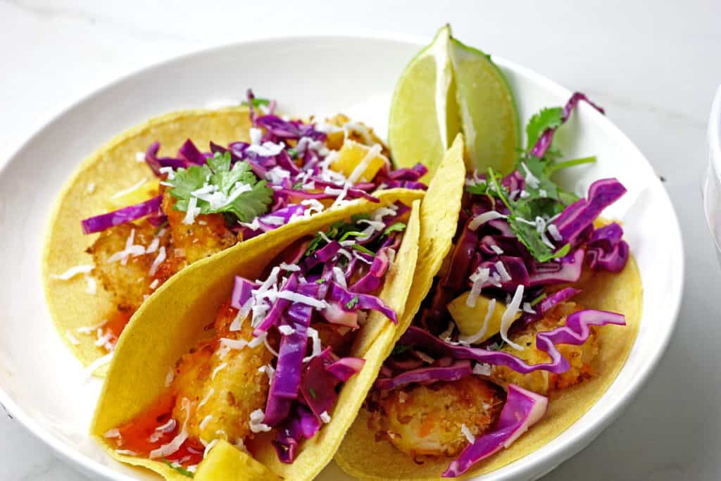 Air fryer coconut shrimp tacos on a white background.