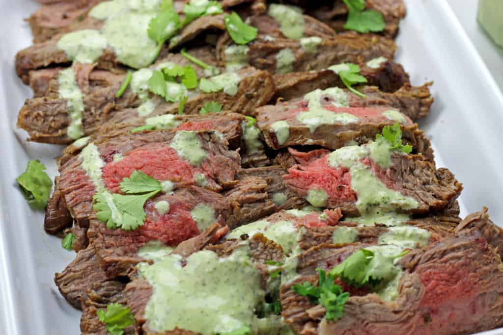 Close of instant pot carne asada on a platter with cilantro garlic sauce drizzled on top.