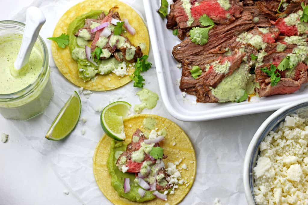 Platter of Instant Pot Carne Asada sliced up with cilantro garlic sauce and tacos on the side.