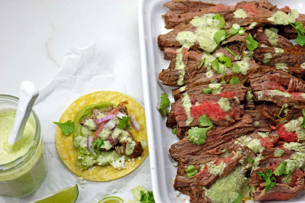 Platter of Instant Pot Carne Asada sliced up with cilantro garlic sauce and tacos on the side.