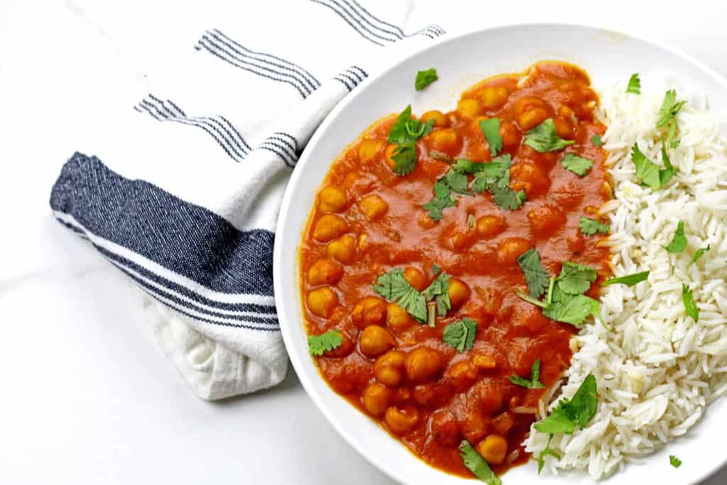 Vegan tikka masala with rice on a white background with a blue and white towel.