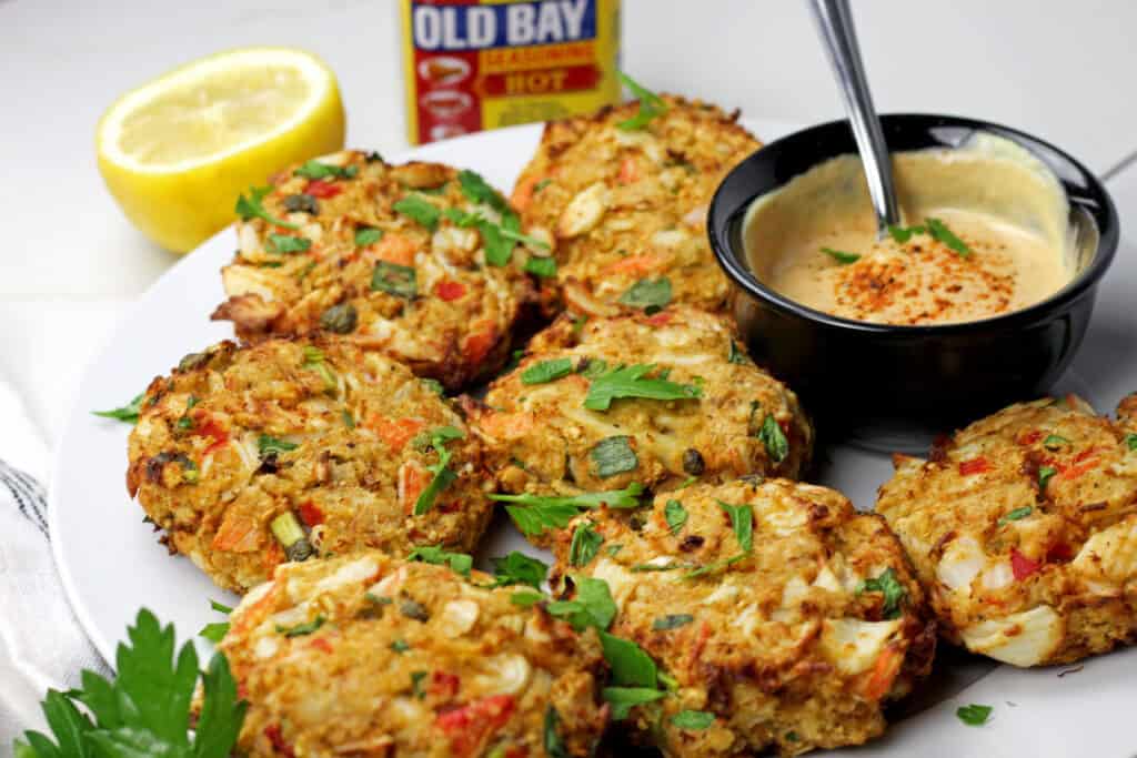 Close up of air fryer crab cakes with a sauce with Old Bay Seasoning in the background