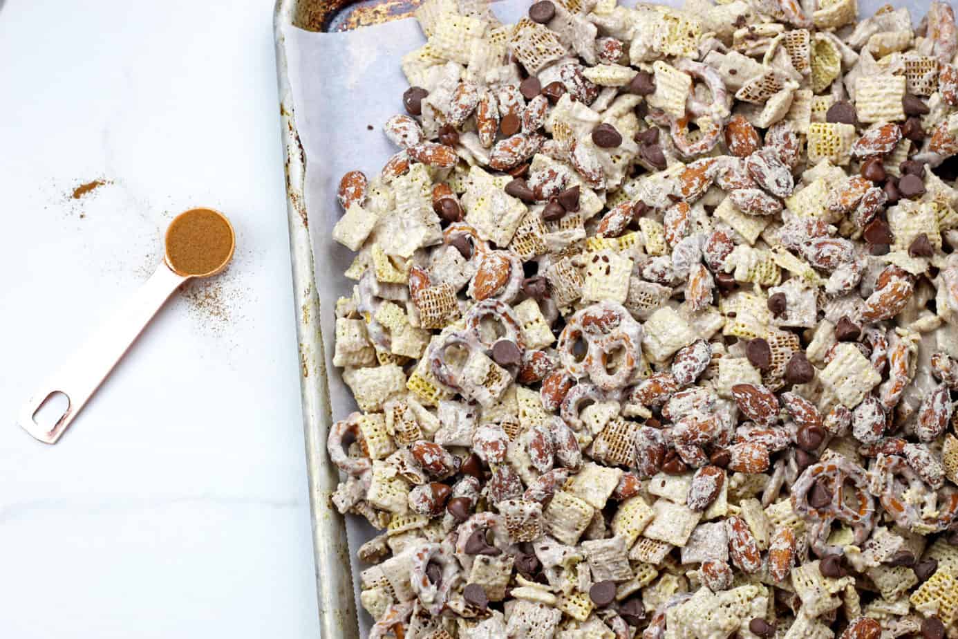 Sheet pan of churro chex mix with a spoonful a cinnamon next to it.