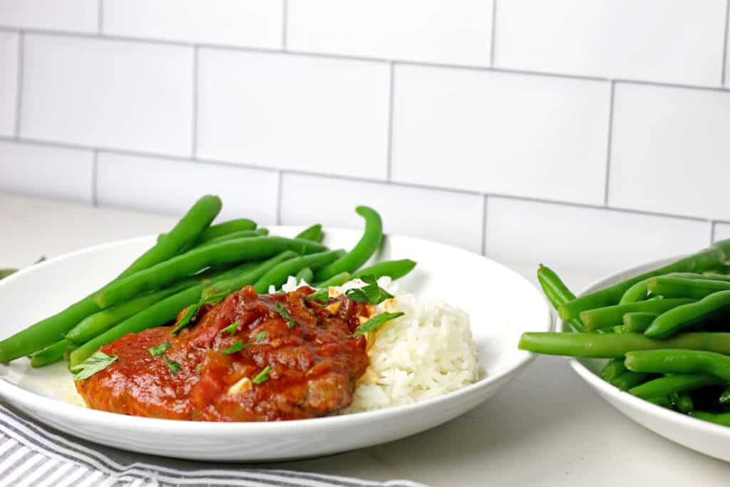 A plate of instant pot swiss steak with green beans and rice on a countertop.