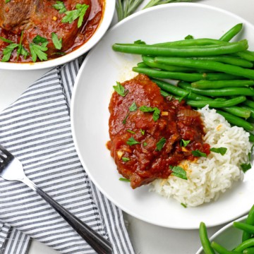 A plate of instant pot swiss steak with green beans and rice on a countertop.